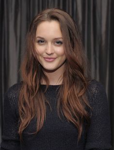 a woman with long brown hair smiling at the camera while standing in front of a black curtain