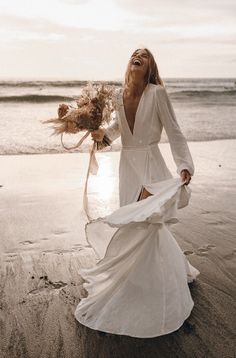 a woman in a white dress is walking on the beach with her hair blowing in the wind