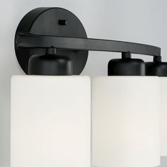 two light bathroom fixture with black finish and white glass shades on the top, against a gray background