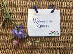 a welcome to my garden sign and flowers on a wicker tablecloth with blue handles