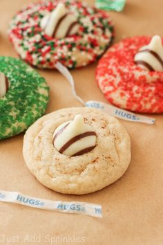 four decorated cookies sitting on top of a brown paper wrapper with white and red sprinkles