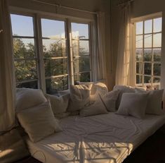 a bed sitting in front of two windows with white pillows on top of each one