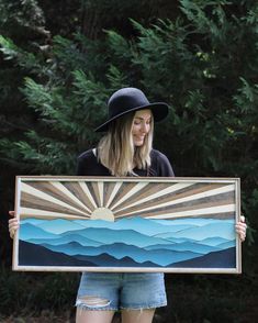 a woman holding up a painting in front of trees