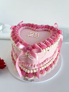 a heart - shaped cake with pink icing and pearls on the bottom is decorated with a number twenty