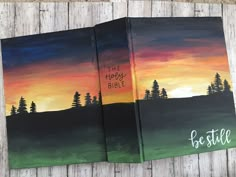 two bibles with the words be still painted on them and trees in the background