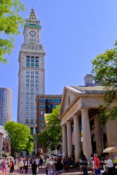 people are walking around in front of a tall building with a clock on the top