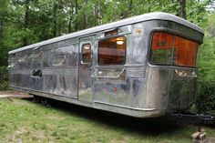 an old trailer is parked in the grass near some trees and bushes with its door open