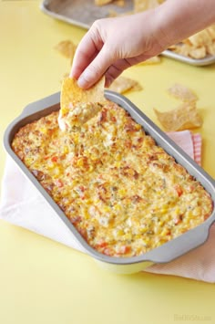 a person dipping a tortilla chip into a casserole dish