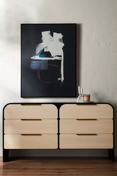 an abstract painting hangs on the wall above a dresser