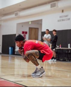 a man in red shirt and black hat crouching on basketball court with other people watching