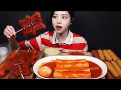 a woman holding up two skewers of food over a table with other foods on it