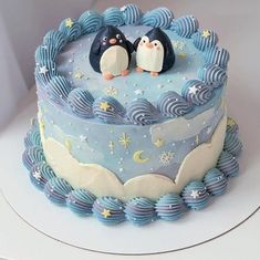 there is a cake with two penguins on top and blue icing around the edges