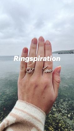 a woman's hand with two rings on it near the water and a pier