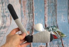 a hand holding a crocheted object on top of a wooden table next to a white ball