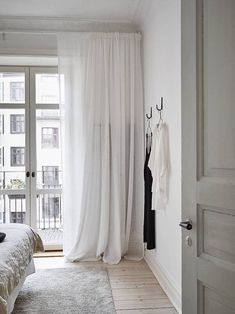 a bedroom with white walls and flooring has a large window that looks out onto the street