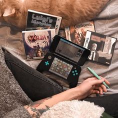 an orange cat laying on top of a bed next to a person holding a nintendo wii game system