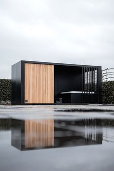 a black building with a wooden door on the side and water in front of it