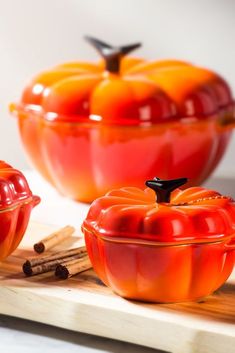 an orange glass dish with two pieces of fruit in it on a cutting board next to cinnamon sticks