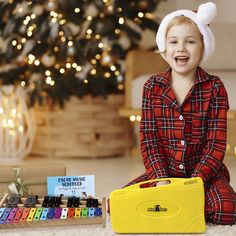 a young boy sitting on the floor next to a christmas tree with an assortment of crayons in front of him