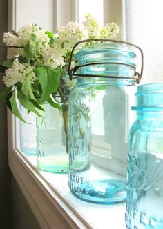 three mason jars sitting on a window sill with flowers in the vases next to them