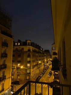 a city street at night with cars parked on the side and buildings in the background