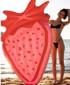 a woman standing on the beach next to an inflatable strawberry shaped object that looks like a heart