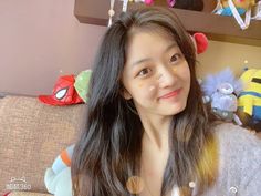 a woman with long hair sitting on a couch in front of stuffed animals and toys