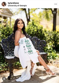 a woman is sitting on a bench in a white dress with green writing on it