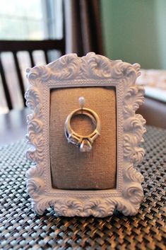 a white frame with a ring on it sitting on top of a table next to a chair