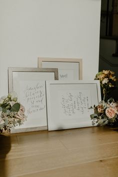 three framed pictures sitting on top of a wooden table next to vases and flowers