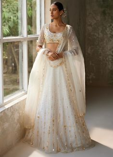 Embrace timeless elegance with the exquisite Ivory Embroidered Lehenga Set, crafted from pure silk organza. The full-length ivory lehenga showcases intricate hand-embroidery, adding a touch of opulence and tradition to the ensemble. Delicate motifs dance across the ethereal fabric, shimmering subtly in the light. Paired with matching half sleeved blouse features meticulous hand-embroidery, enhancing its luxurious appeal. A beautifully completed dupatta with hand-embroidered borders and motifs th Ethereal Fabric, Ivory Lehenga, Lehenga Dupatta, Organza Lehenga, Net Lehenga, Vacuum Storage, Intimate Wedding Ceremony, Half Sleeve Blouse, Embroidered Lehenga