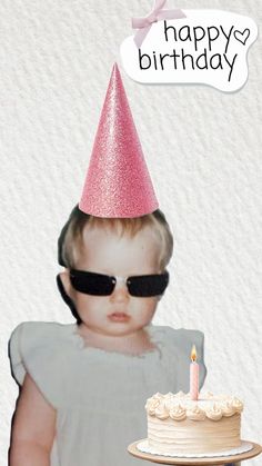 a baby wearing sunglasses and a pink hat with a birthday cake in front of it