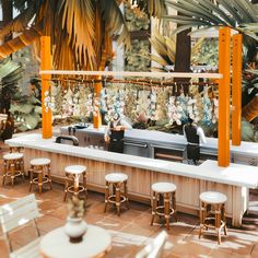 an outdoor bar with white stools and palm trees in the backgrounge