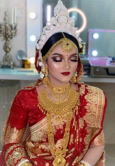 a woman in a red and gold bridal outfit with jewelry on her head sitting down