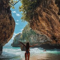 a woman standing on the beach in front of some rocks