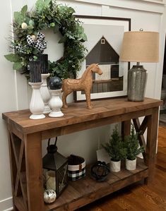 a wooden table topped with a horse figurine next to a lamp and wreath