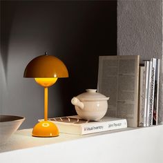 an orange lamp sitting on top of a table next to a white bowl and book