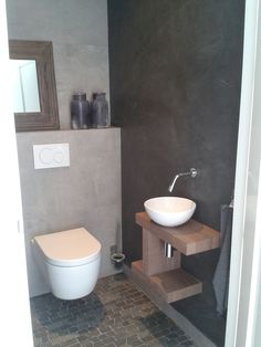 a white toilet sitting next to a sink in a bathroom under a wooden mirror mounted above it