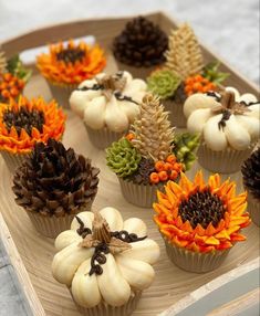 cupcakes decorated with fake sunflowers and pine cones on a wooden tray