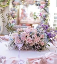 a table topped with pink and purple flowers next to a wine glass on top of a table