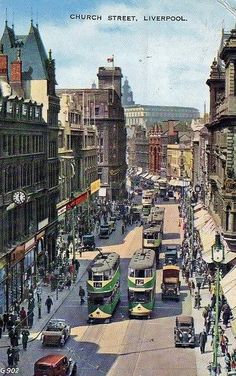 there are many buses and cars on the street in this old time photo, as well as people walking down the sidewalk