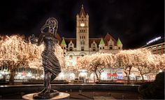 there is a statue in front of a building with lights all around it and the clock tower