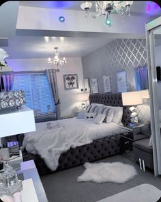 a bedroom decorated in silver and white with chandelier above the bed, mirror on the wall