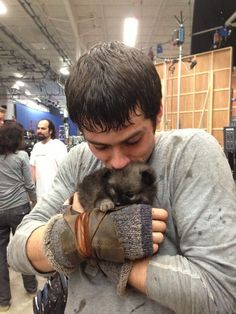 a man holding a small animal inside of a building with other people in the background