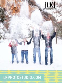 four people are standing in the snow with their arms up and one person is throwing snow into the air