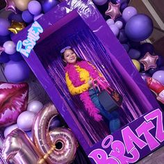 a woman standing in front of a purple box surrounded by balloons