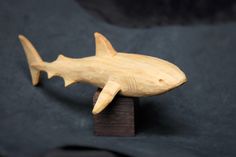 a carved wooden shark sitting on top of a piece of wood next to a black background