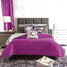 a bed with purple sheets and pillows on top of it next to a night stand