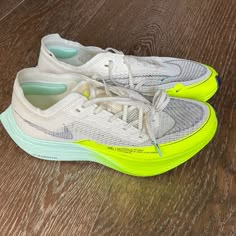 a pair of white and yellow sneakers on a wooden floor with light green soles