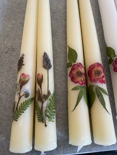 four white candles decorated with flowers and leaves on top of a gray countertop next to each other